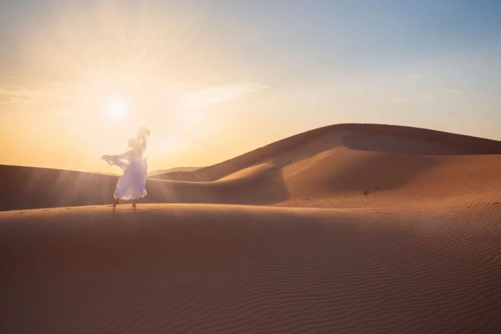Femme en robe blanche dansant pieds nus sur les dunes au lever du soleil dans le désert marocain