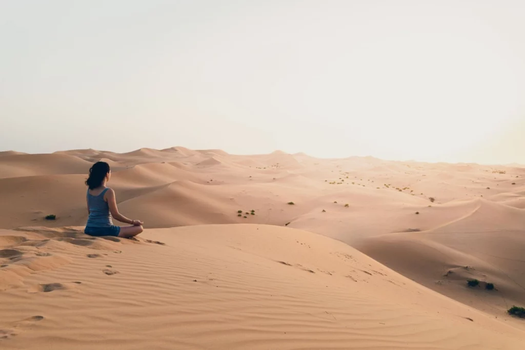 Femme méditant seule sur les dunes dorées du désert marocain au lever du soleil