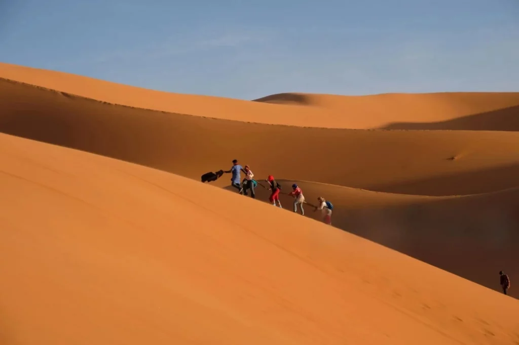 Groupe de randonneurs gravissant les dunes guidés par un chamelier dans le désert marocain